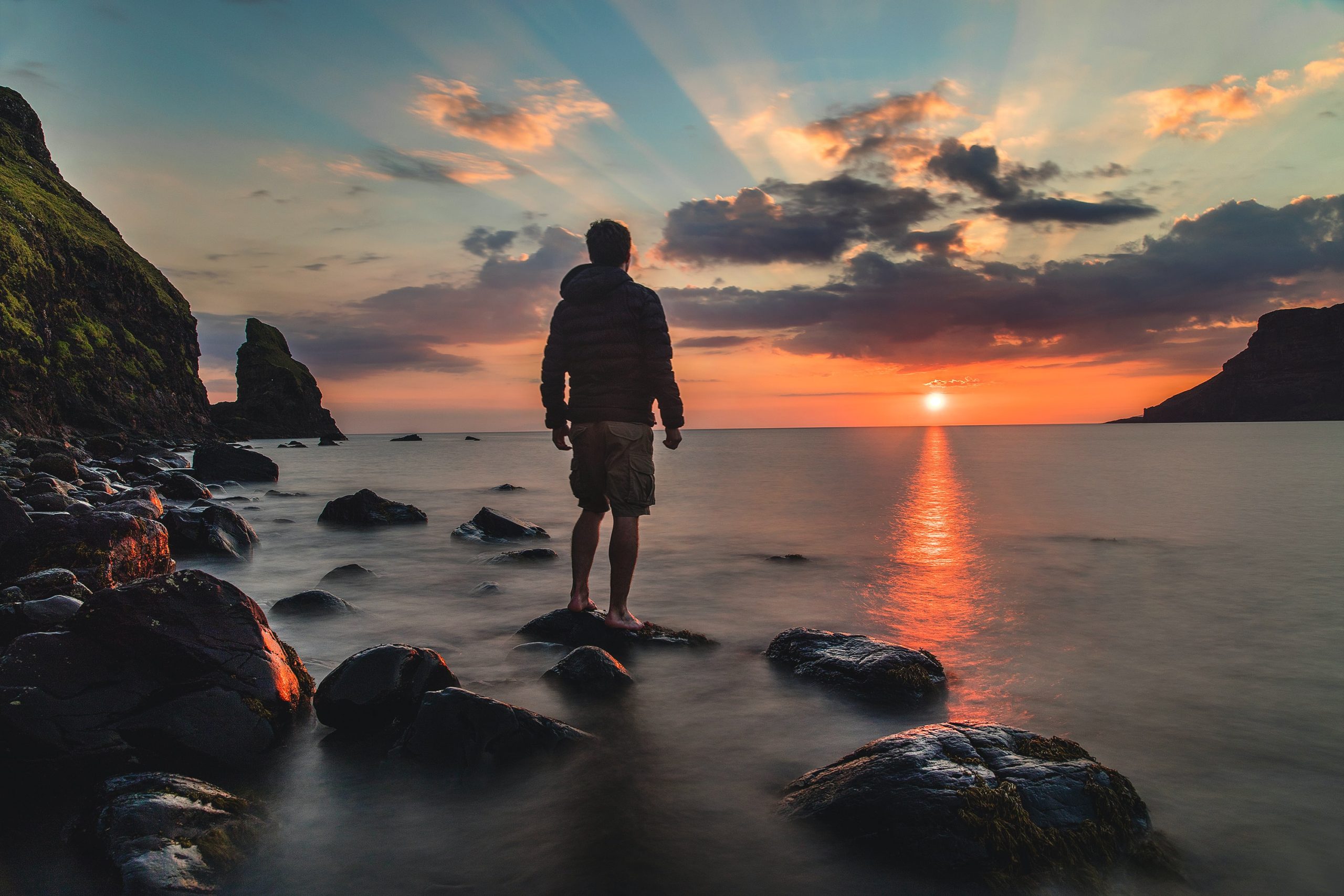 Man Standing with his Back Turned on a Rock in the Water Looking At The Sunset